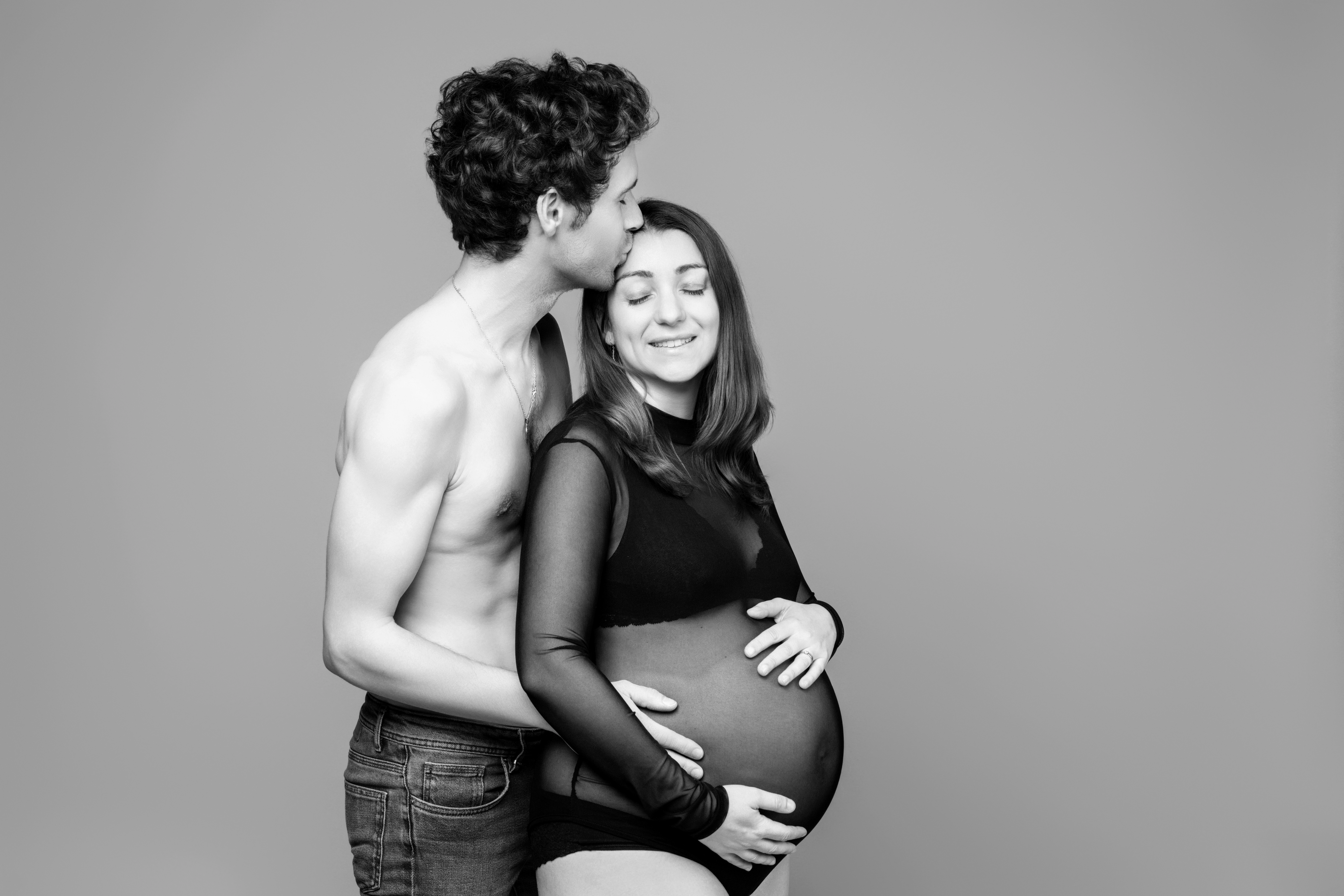 Couple en séance photo grossesse en studio, homme embrassant le front de la femme enceinte, portrait noir et blanc à Châteaugiron